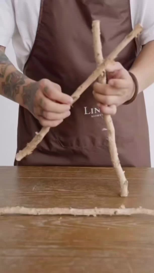 This may contain: a man is making something out of sticks on a wooden table with an apron over his shoulder