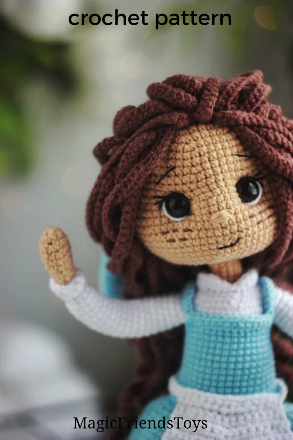 This may contain: a crocheted doll with long brown hair and blue dress holding her arms in the air