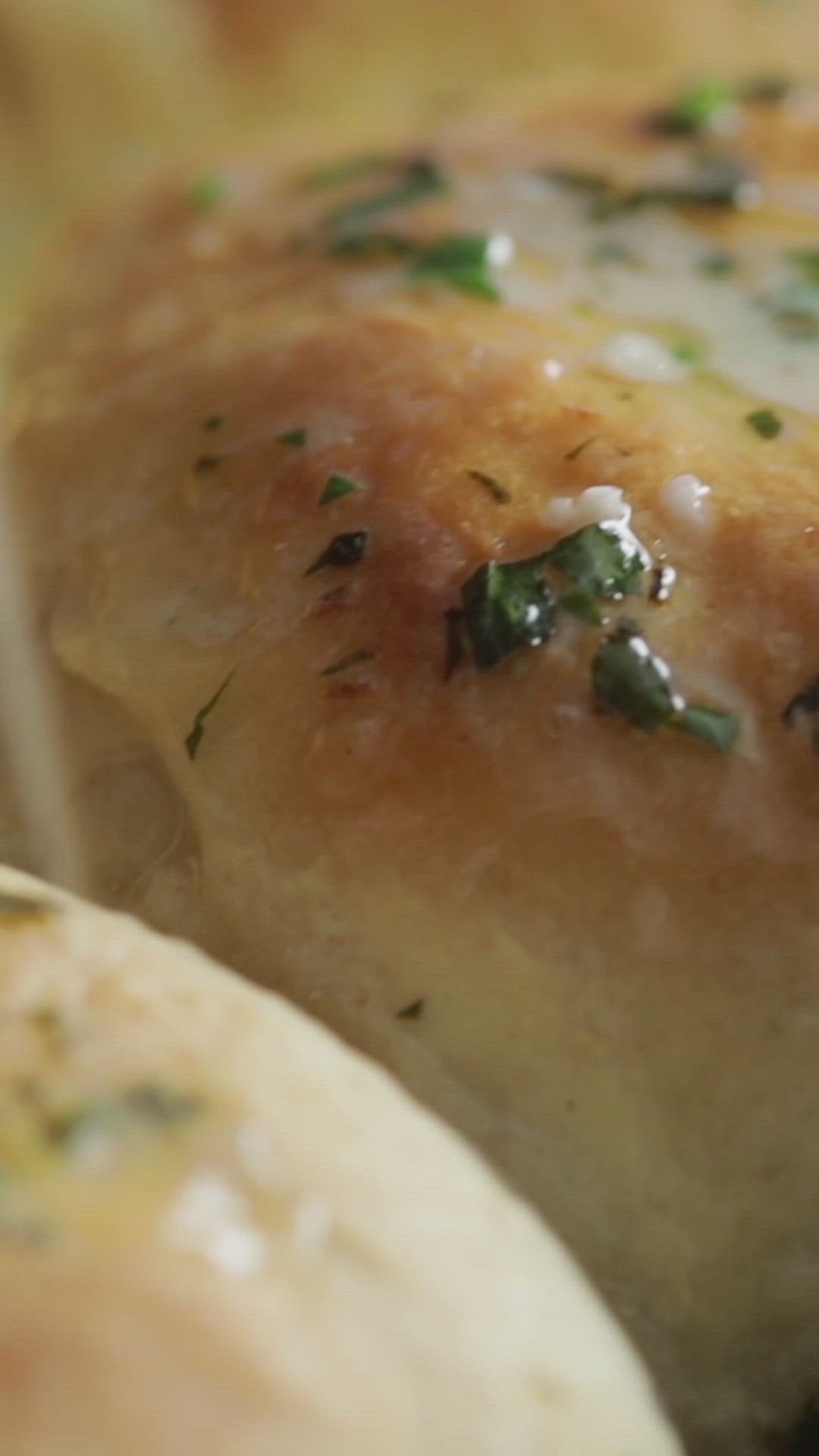 This may contain: a person holding a brush in a skillet filled with bread rolls and cheeses