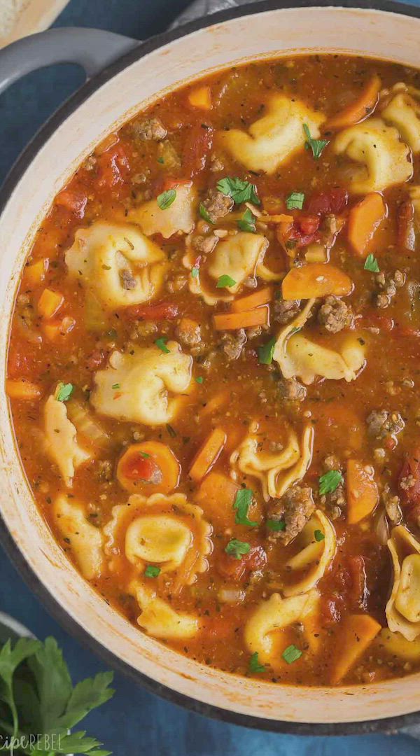 This may contain: a pot filled with pasta and meat soup on top of a blue table next to bread