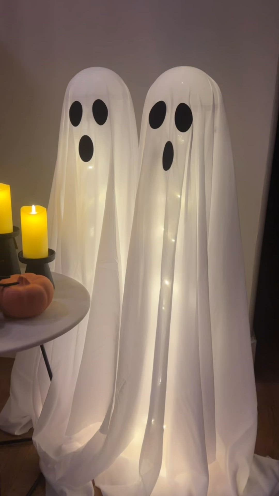 This may contain: two white ghost statues sitting next to each other with candles in front of them on a table