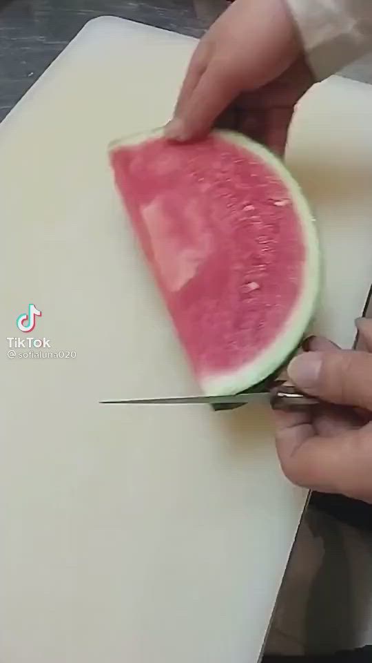 This may contain: a person cutting up a piece of watermelon on top of a cutting board