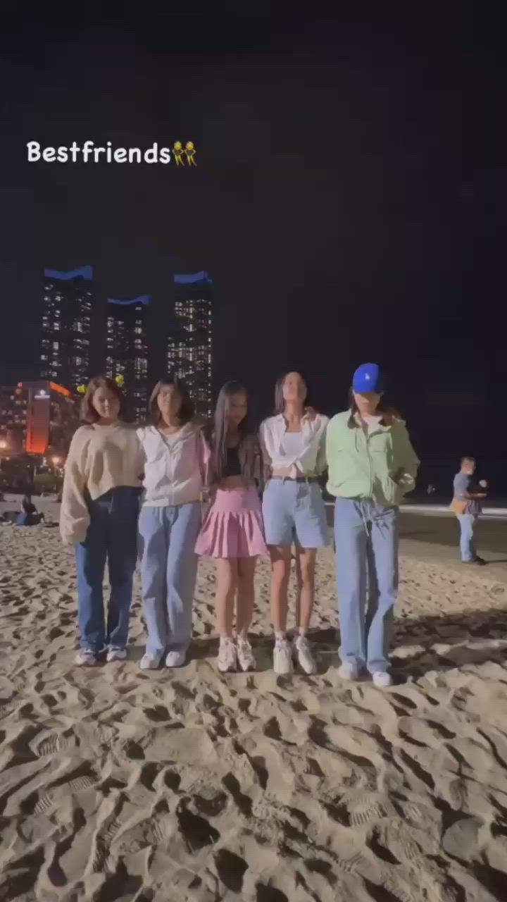 This may contain: four people standing on the beach at night with their arms around each other's shoulders