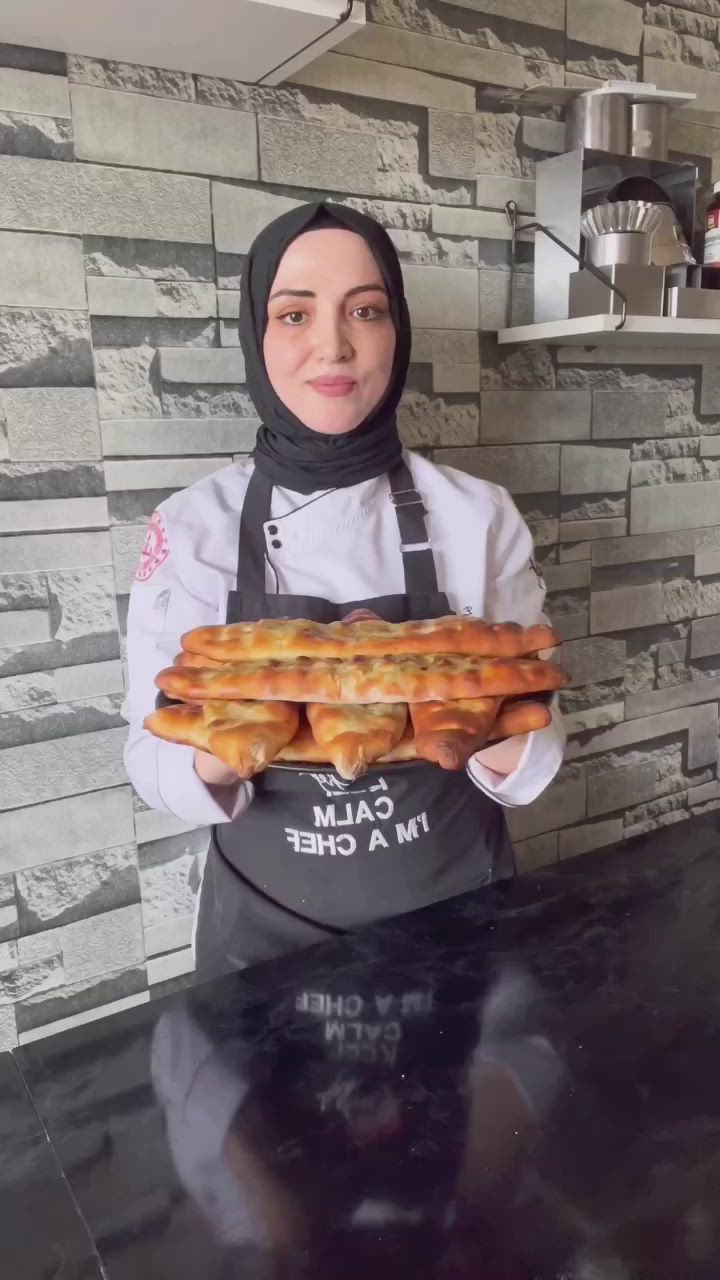 This may contain: a woman holding a tray of bread in front of her face with the words kr pidesi tarif on it