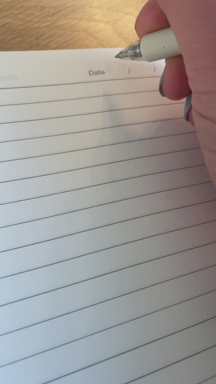 This may contain: a person holding a pen and writing on a piece of paper with lined lines in it