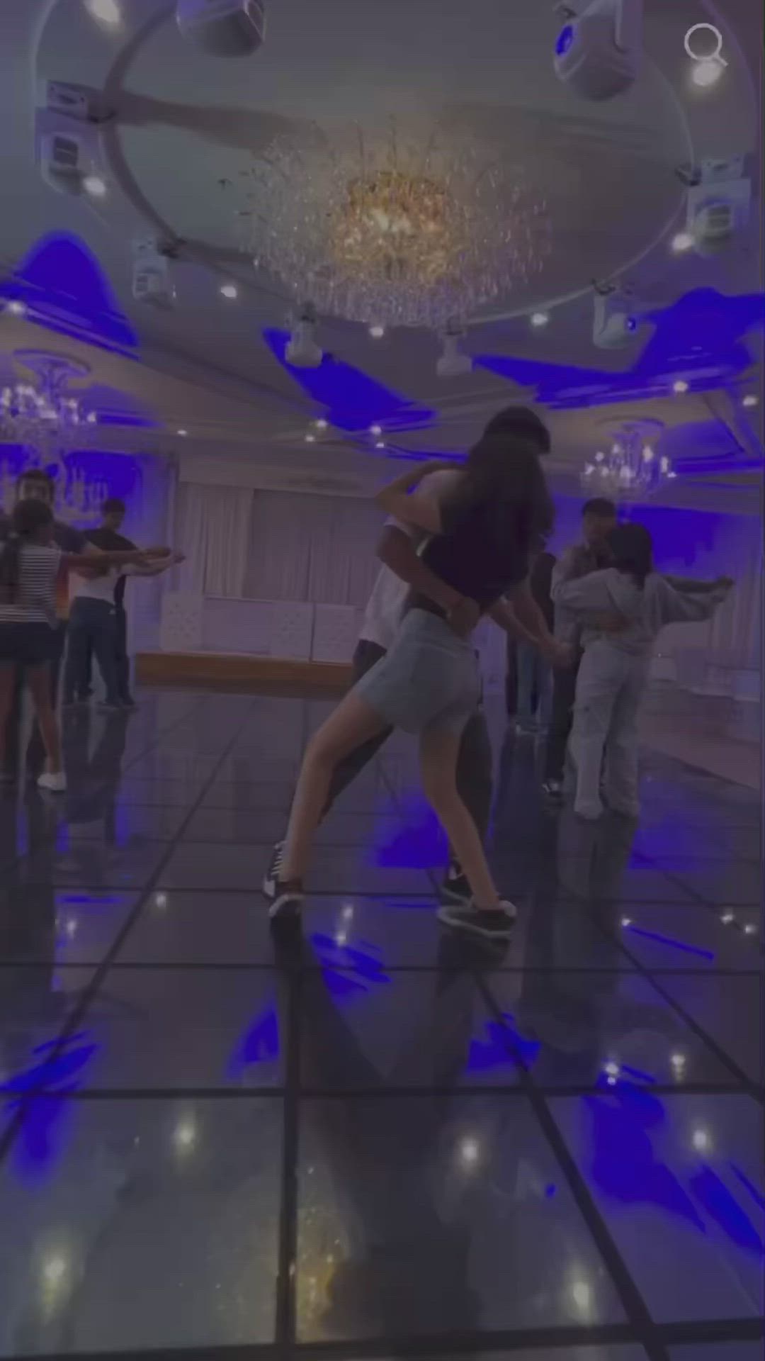 This may contain: two people are dancing in a large room with blue lights on the ceiling and floor