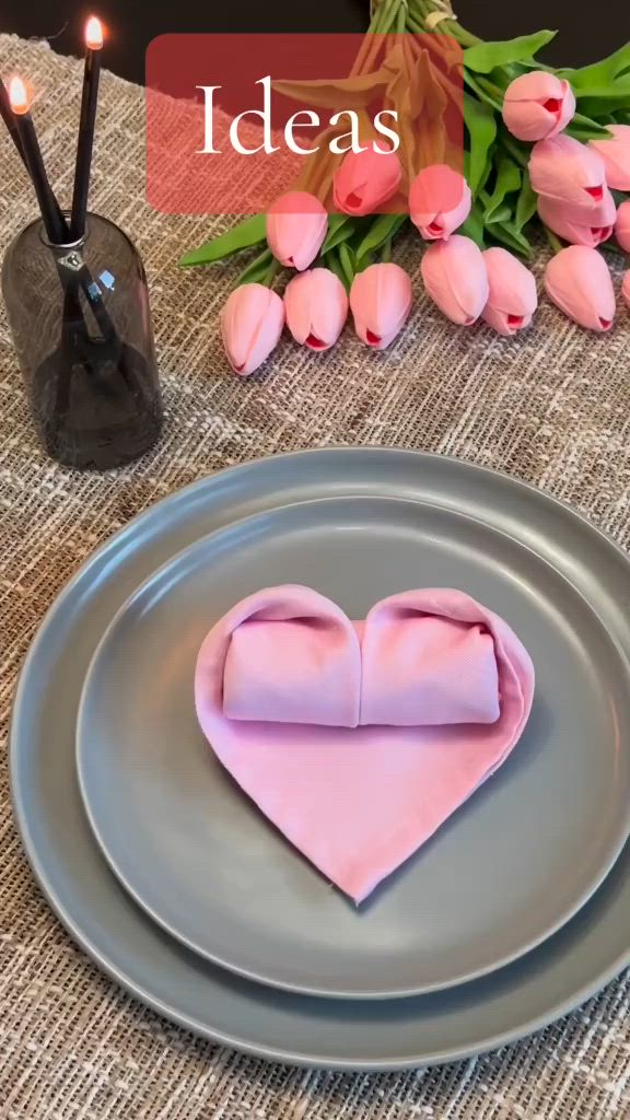 This may contain: a heart shaped cake sitting on top of a plate next to candles and pink flowers