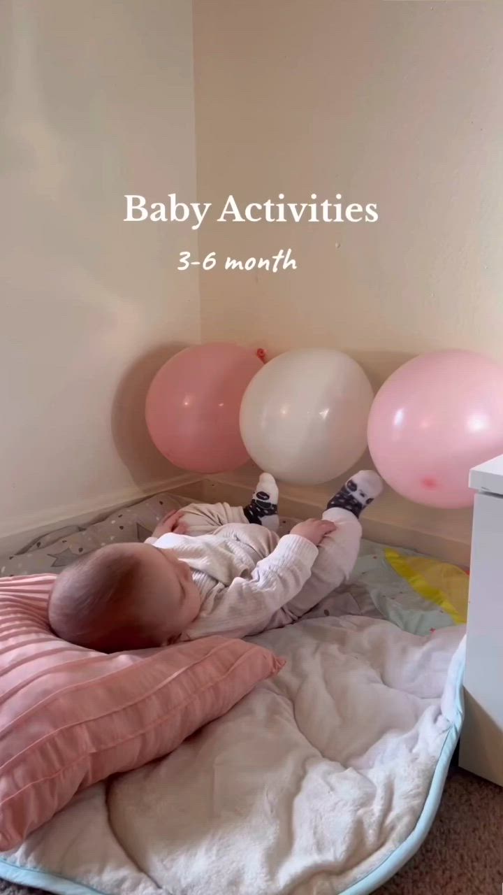 This may contain: a baby laying on top of a bed next to pink and white balloons with the words baby activities 3 - 6 months