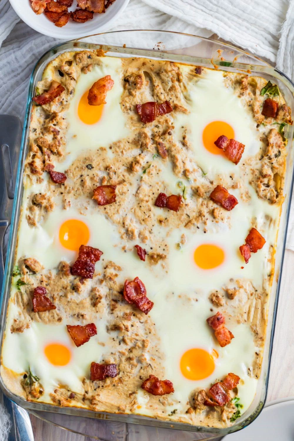 This may contain: keto sausage biscuits and eggs in a casserole dish with bacon on top