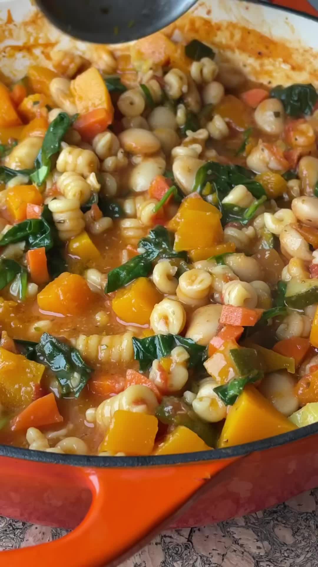 This may contain: a pot filled with pasta and vegetables on top of a table