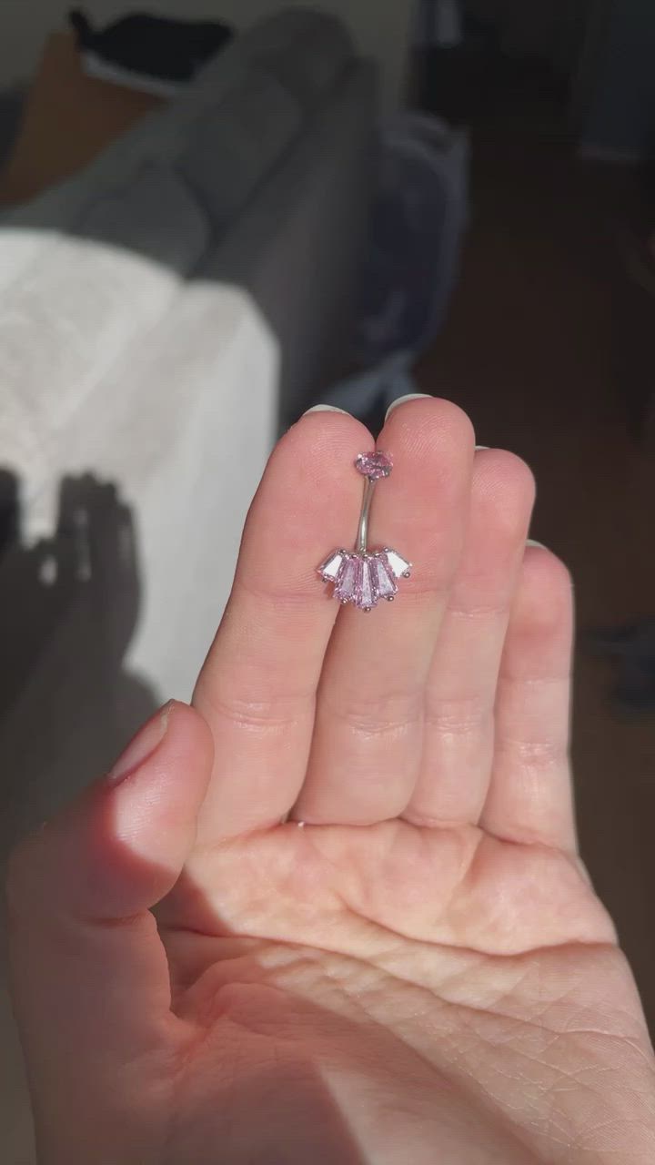 This may contain: a person holding up a pink diamond ring in their hand with the light shining on them