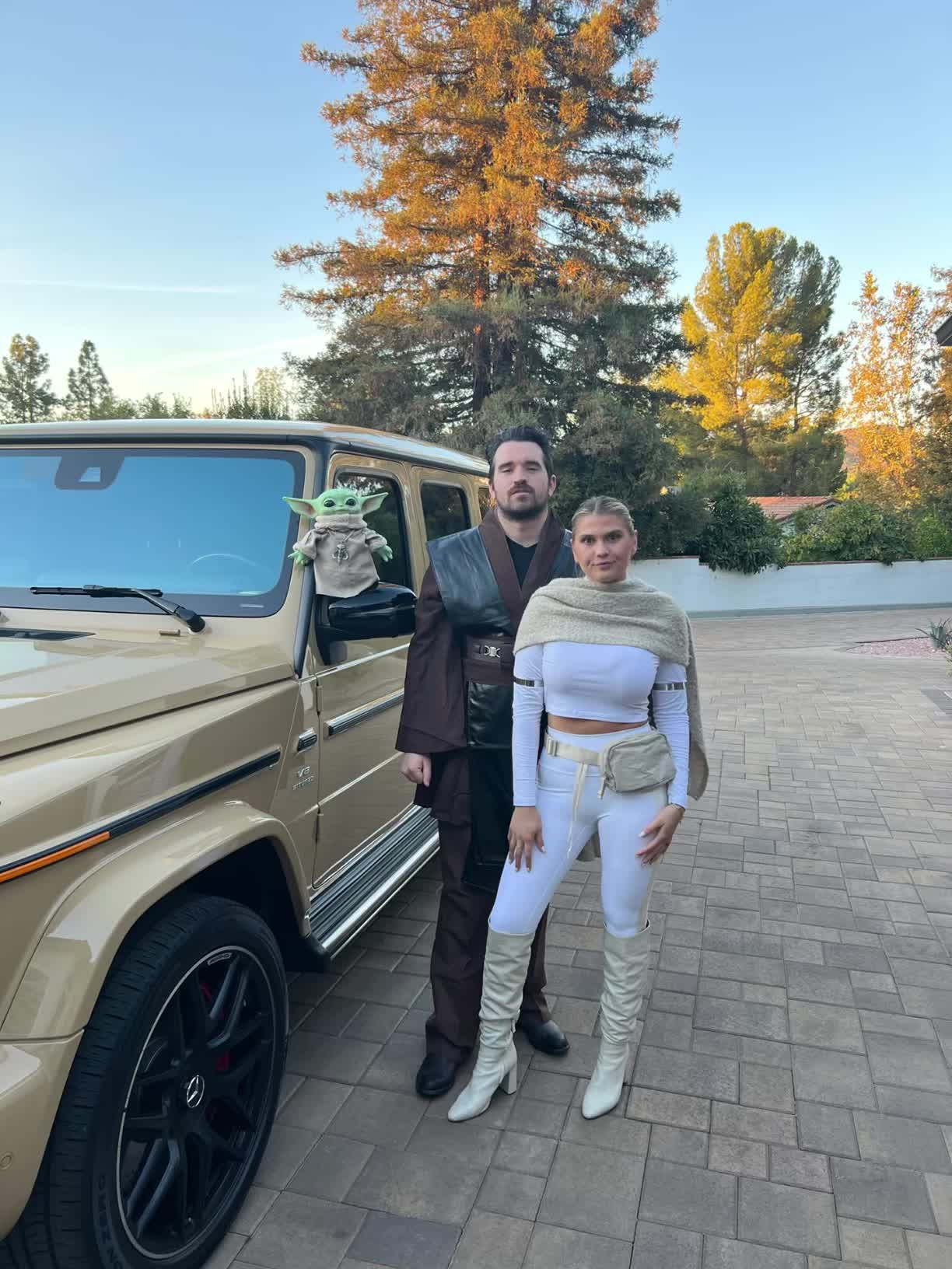 This may contain: a man and woman standing in front of a car giving the peace sign with their hands