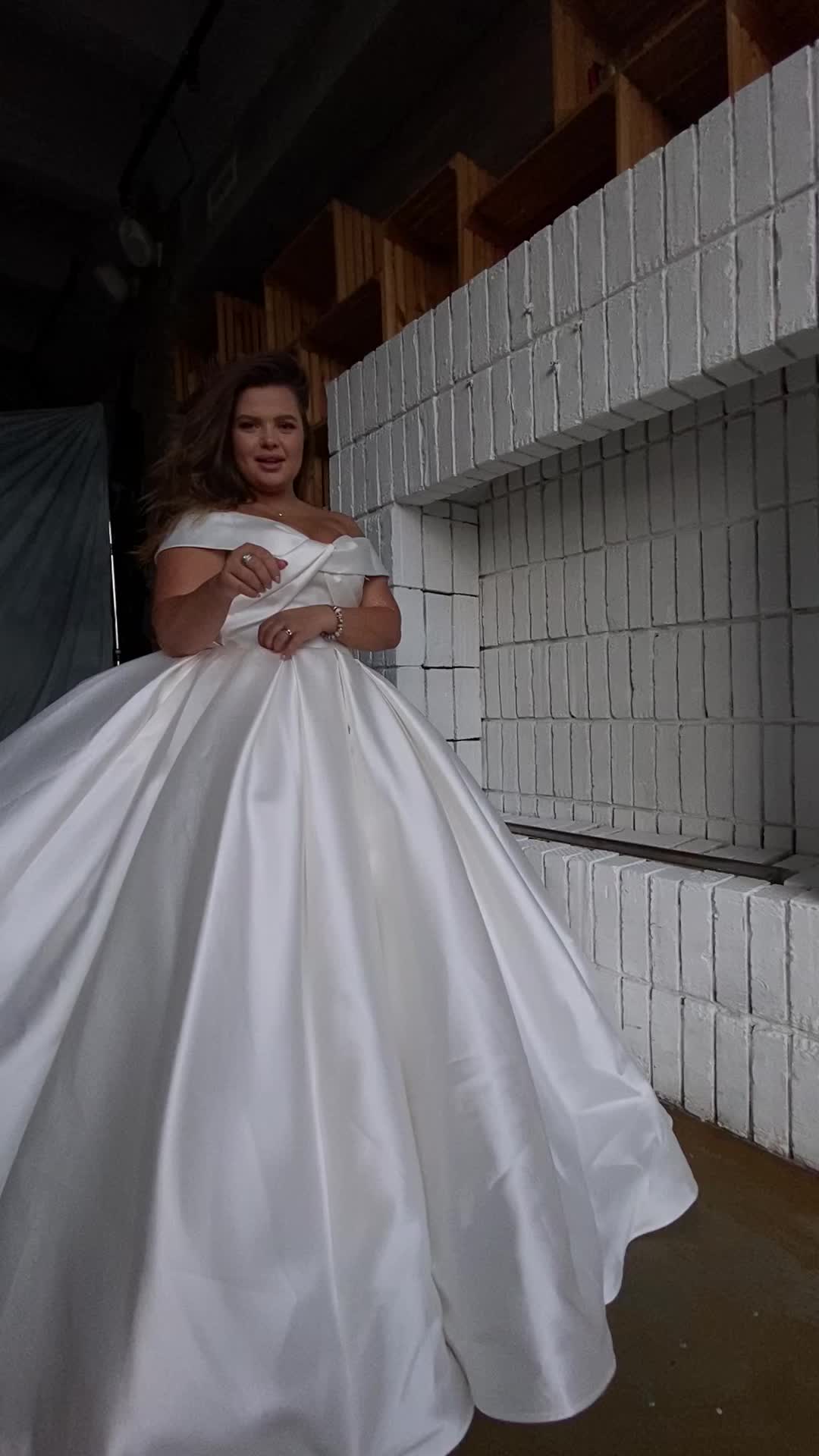 This may contain: a woman in a white wedding dress standing next to a brick wall and posing for the camera