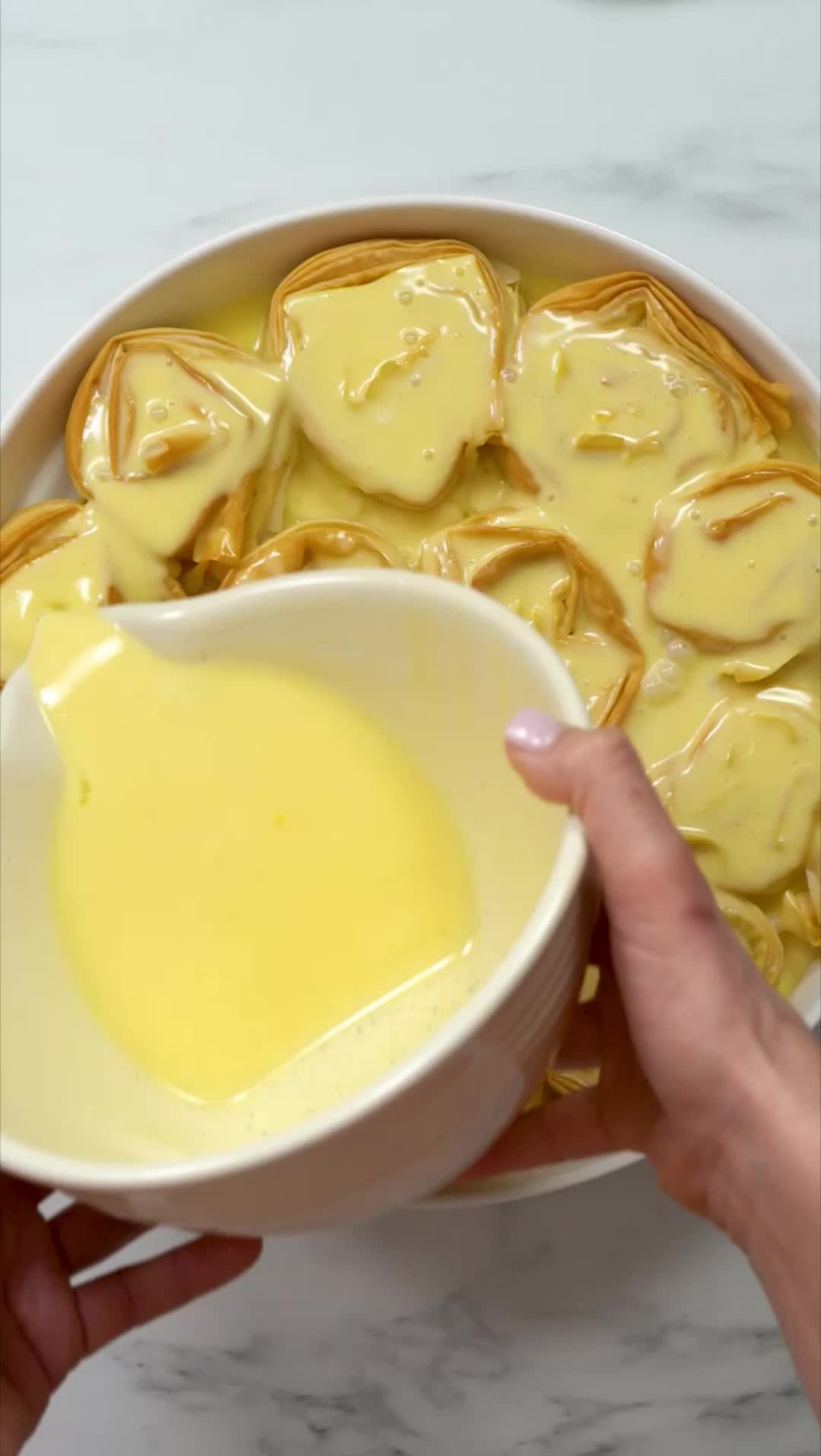 This may contain: a bowl filled with apple pie filo cake on top of a white marble counter