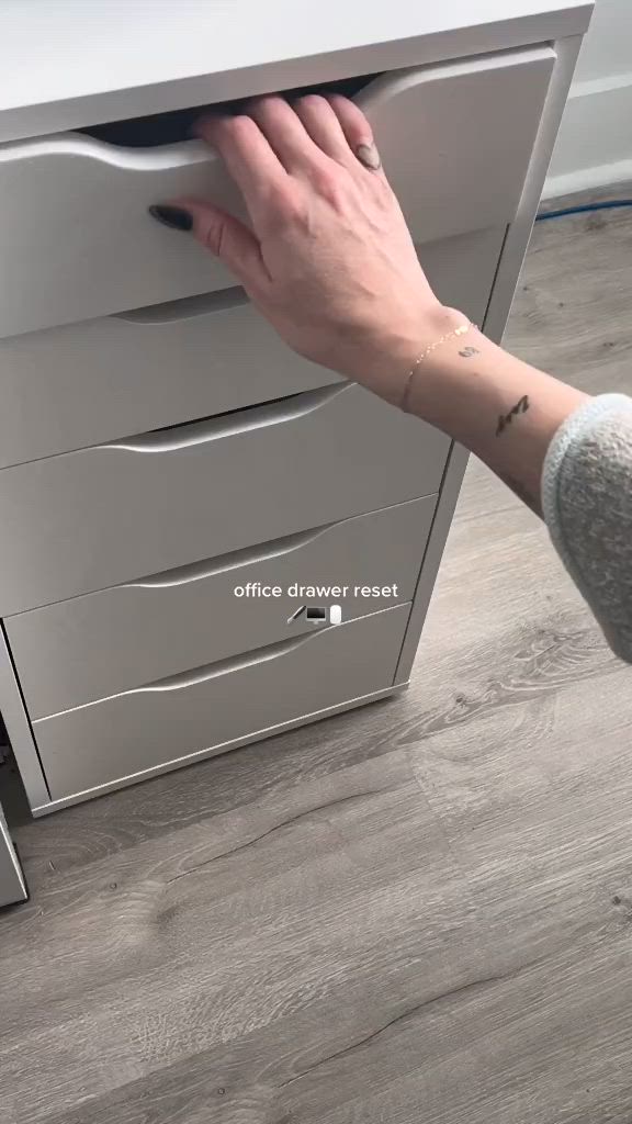 This may contain: a woman's hand reaching for the drawer on a filing cabinet that is open