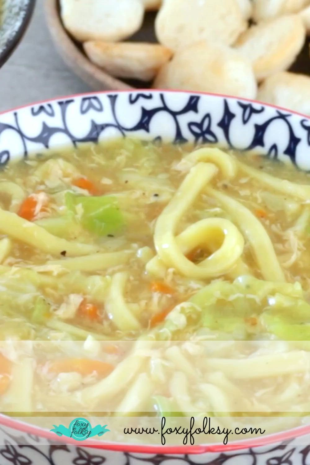 This may contain: a bowl of soup with noodles and carrots in it on top of a table