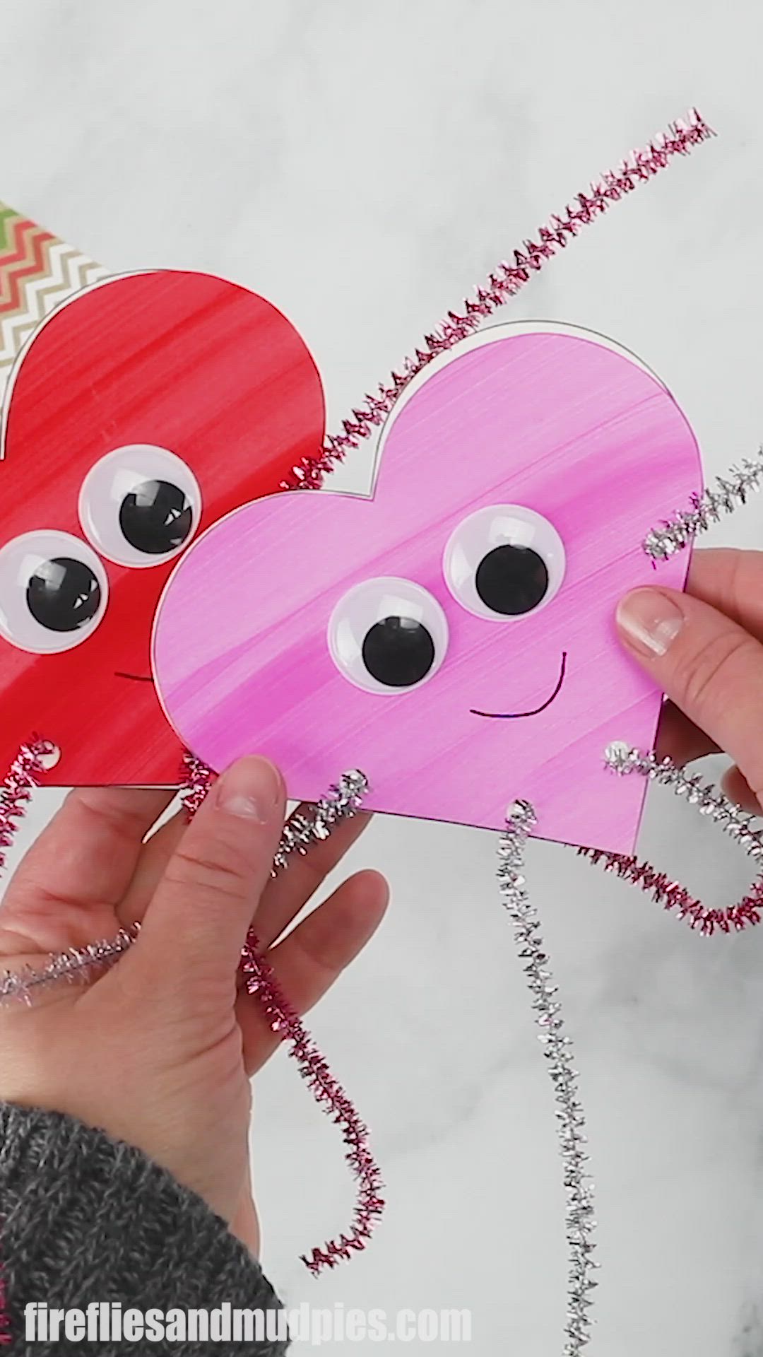 This may contain: two paper hearts with googly eyes are being held by someone