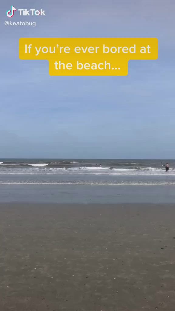 This may contain: two people standing on the beach looking at an object in the sand that says sea - ball