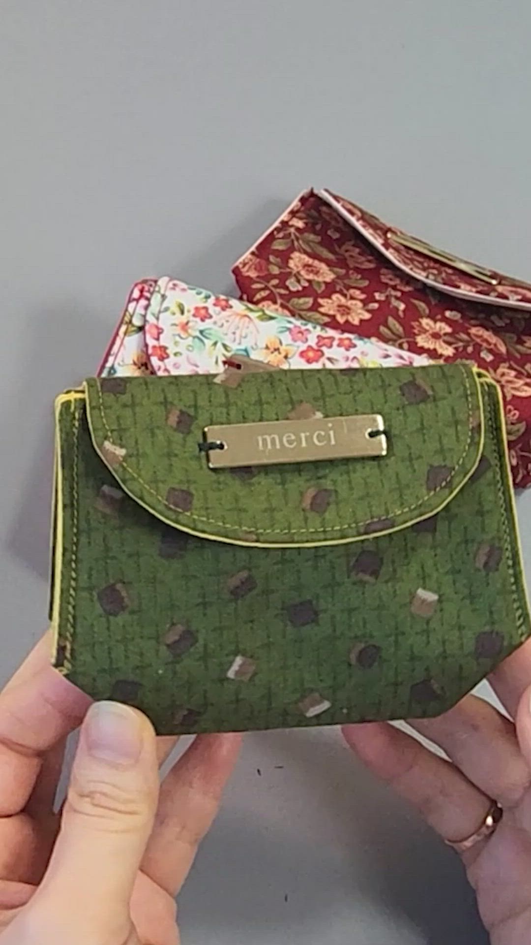 This may contain: a person holding up a green purse with two pieces of fabric on it and the other one has a name plate