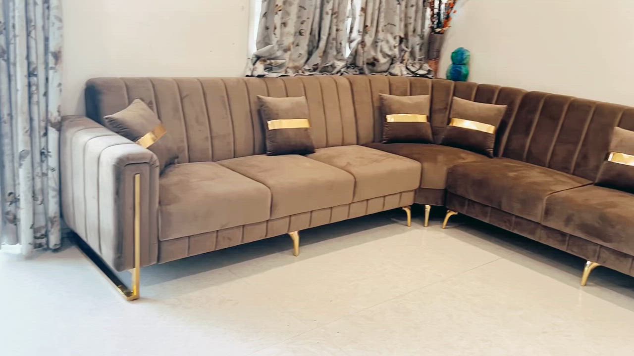 This may contain: a large sectional couch with gold trimmings in a living room next to a window