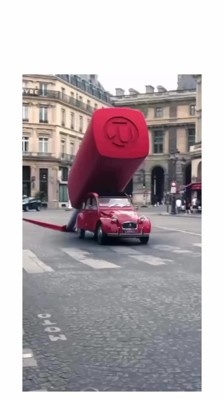 This may contain: a red car driving down a street next to a large object on the back of it's head