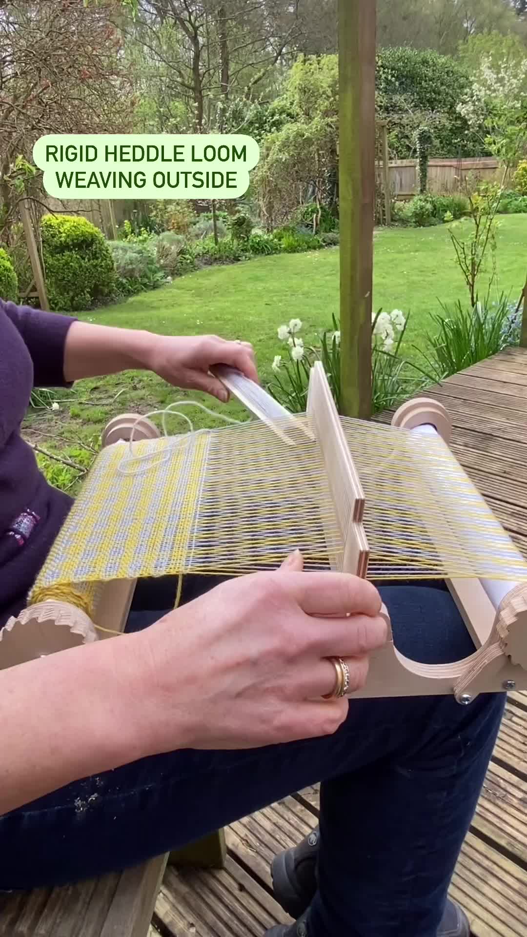 This may contain: a woman is sitting on a bench with an open book in her hand and the words, right middle loom weaving outside