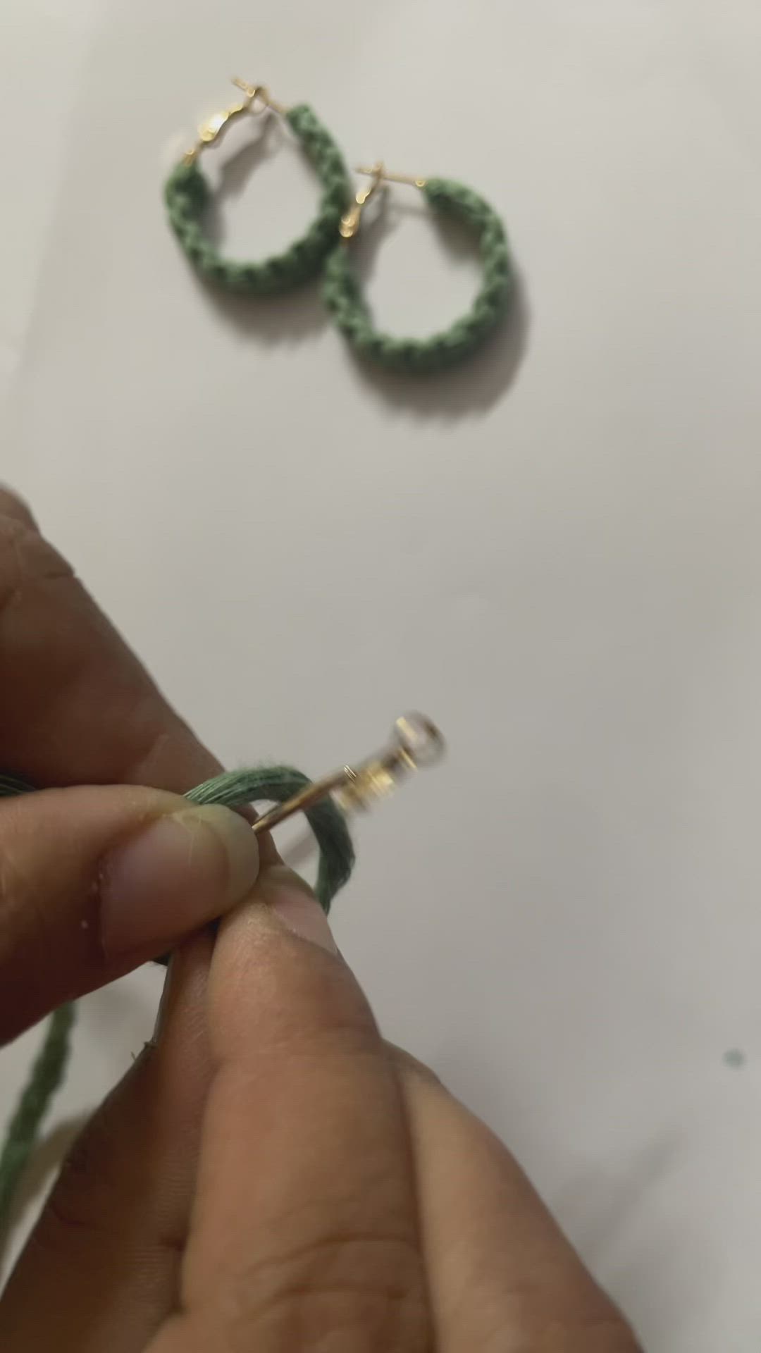 This may contain: someone is working on some green beads with gold hoop earrings attached to the end of each bead