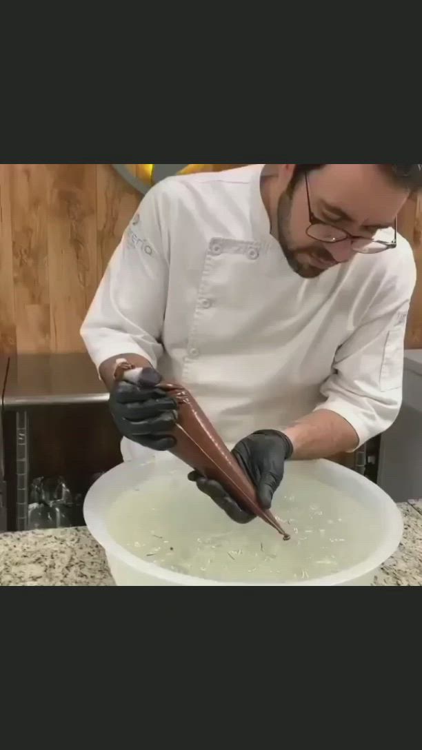 This may contain: a man in white shirt and black gloves preparing food