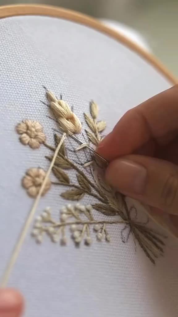 This may contain: someone is stitching flowers on a piece of fabric with a needle in their hand