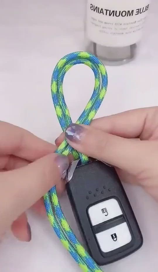 This may contain: someone is tying a car key chain with a blue and green string that has a white button on it