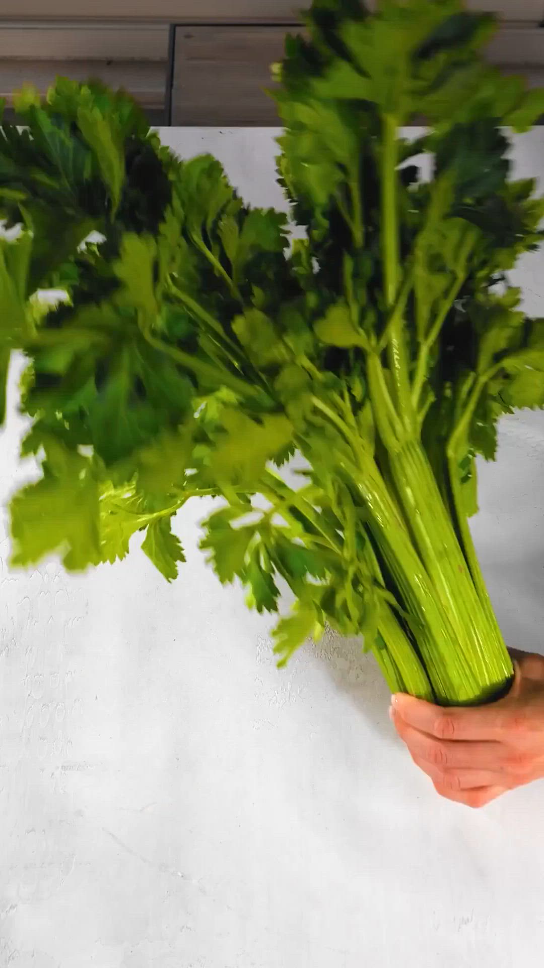 This may contain: a bunch of celery is being held up by someone's hand on a white surface