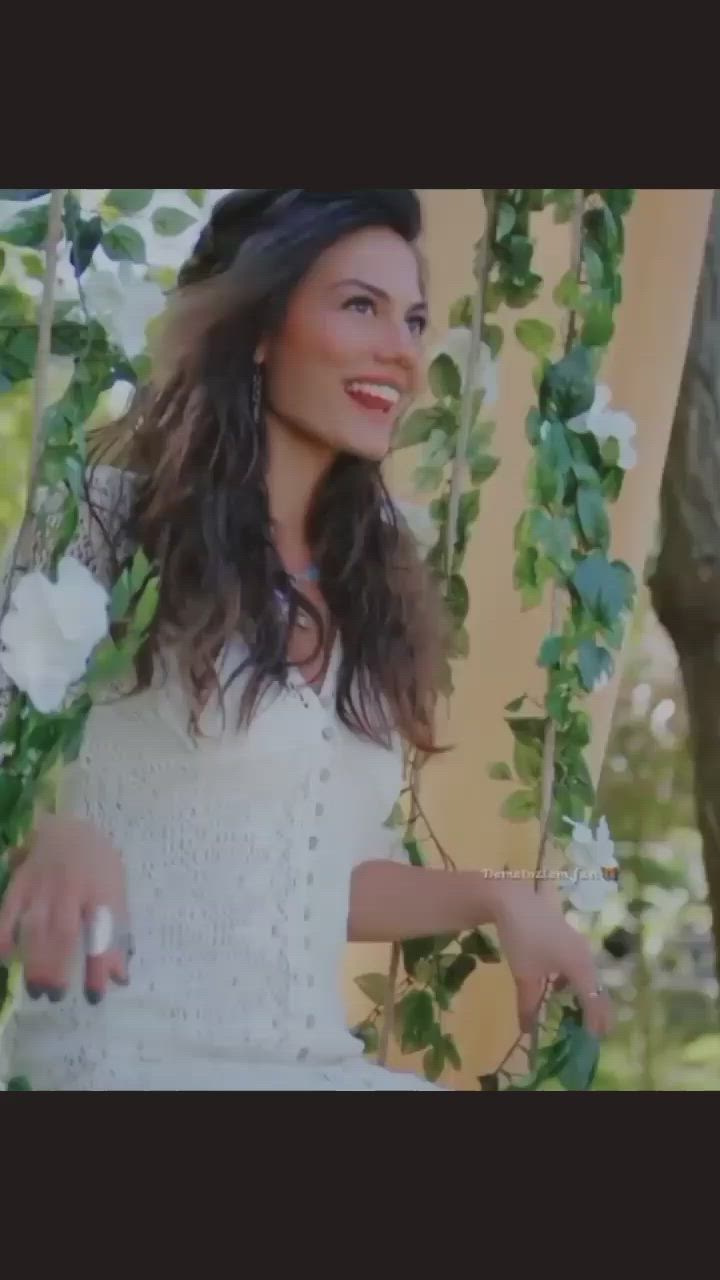 This may contain: a woman wearing a white dress and hat standing in front of a tree with flowers