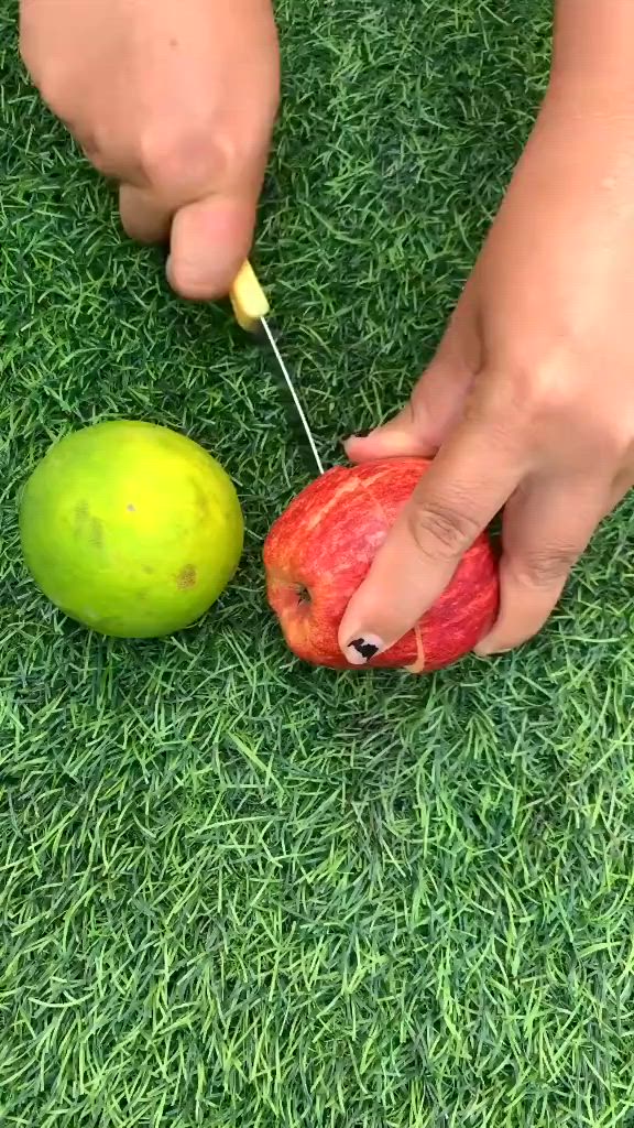 This may contain: a person cutting an apple with a pair of scissors on the grass next to it