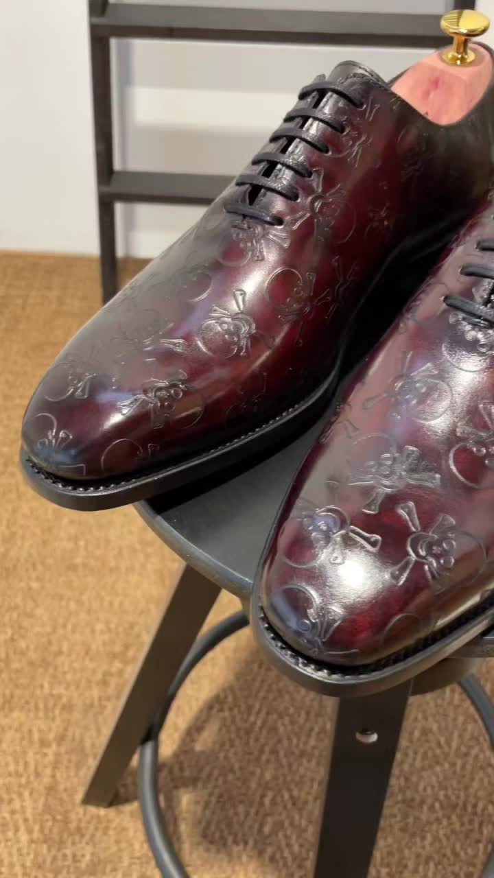 Features our beautiful rosewood burgundy "patina" finish applied by hand, and a 360 degree skull and crossbones motif laser-engraved into the Italian calf leather.  "Patina" is a renowned leather dyeing technique created by Olga Berluti for the famous French brand Berluti in the 80s.  For this pair, our maestro colorist Mario applies the patina in round motions with several different brushes in order to achieve the unique effect pictured.  These beautiful works of art employ the Goodyear Welt, a 150 year old shoemaking process invented by Charles Goodyear Jr in 1869.  The process increases water-resistance and durability, and is known as the gold-standard in the high-end shoe market.  All of our products are hand-made ensuring that no two are ever exactly the same.