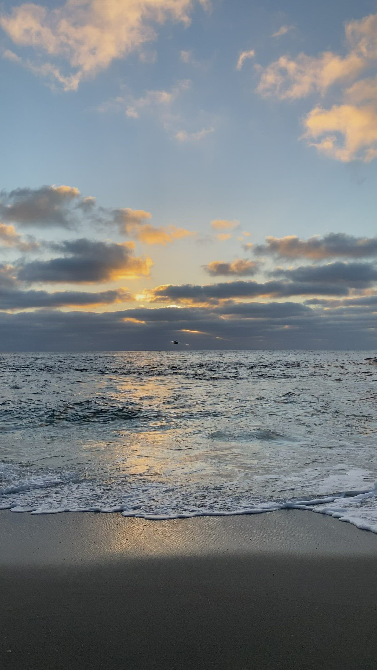 This may contain: the sun is setting over the ocean with clouds in the sky and waves on the beach