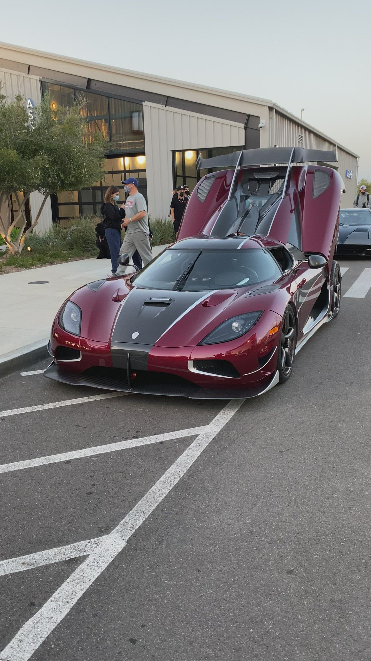 This may contain: a red and black sports car parked in a parking lot next to other cars on the street