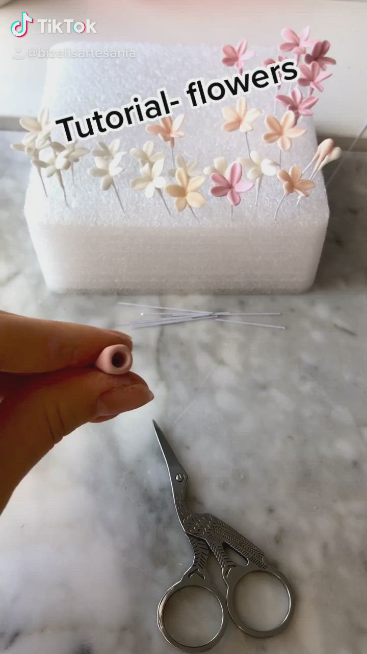 This may contain: a woman's hand holding a pink and white flower shaped ring with two petals on it