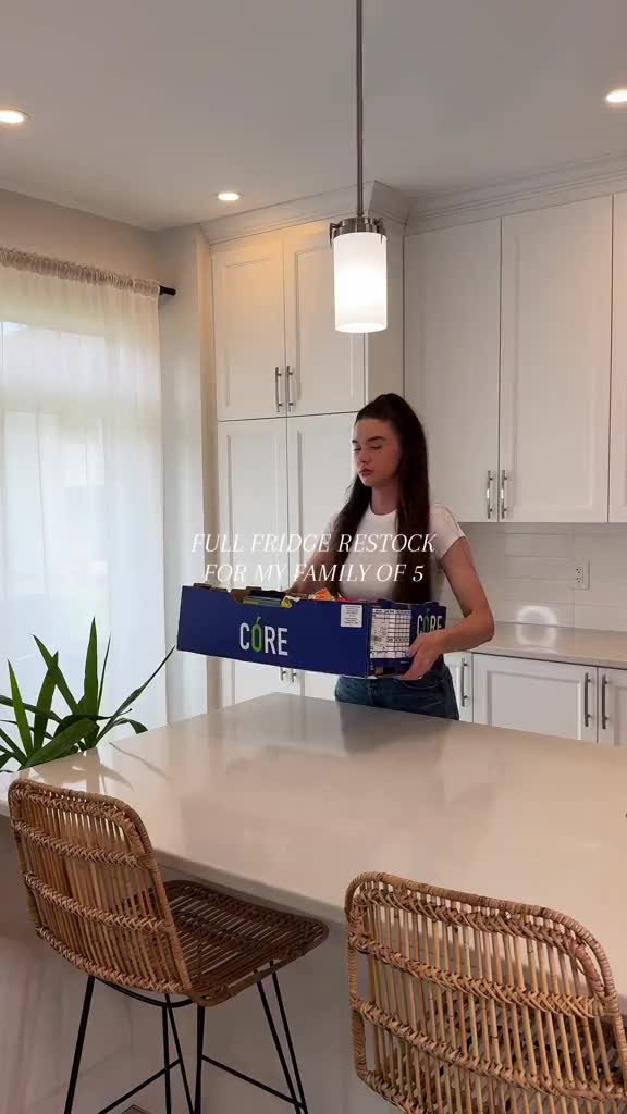 This may contain: a woman sitting at a kitchen counter with an open box of food