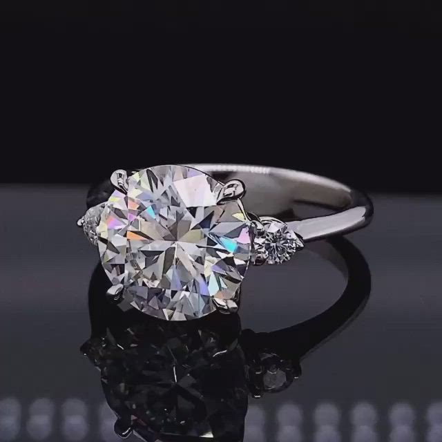 This may contain: a diamond ring with three stones on the top and side, sitting on a reflective surface