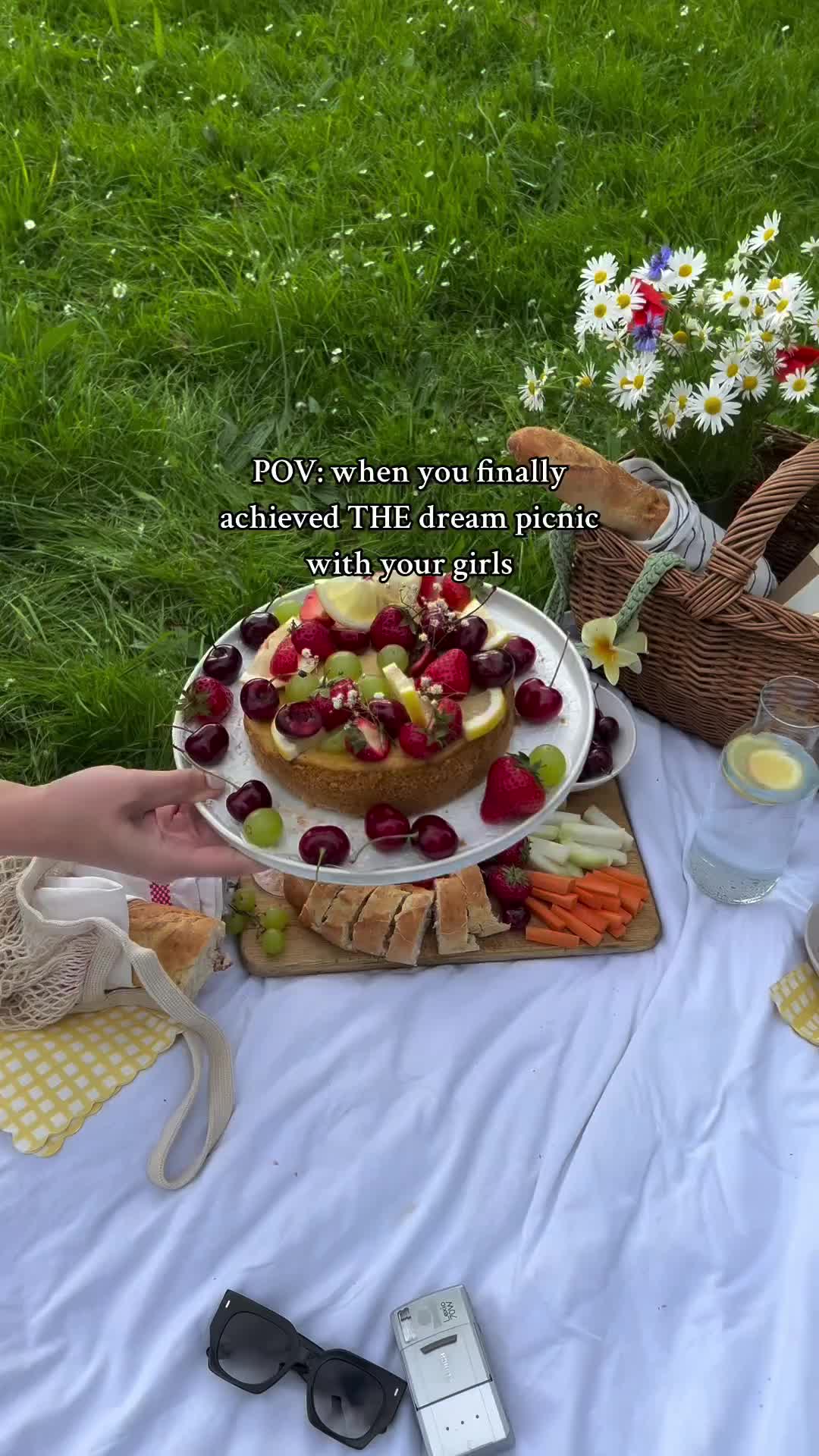 This may contain: a woman is holding a platter with fruit on it and flowers in the background