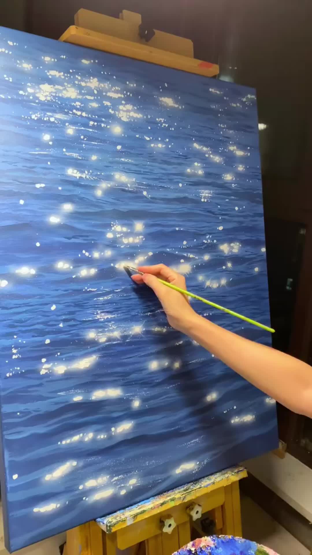 This may contain: a person is painting on an easel with blue water and white stars in the sky