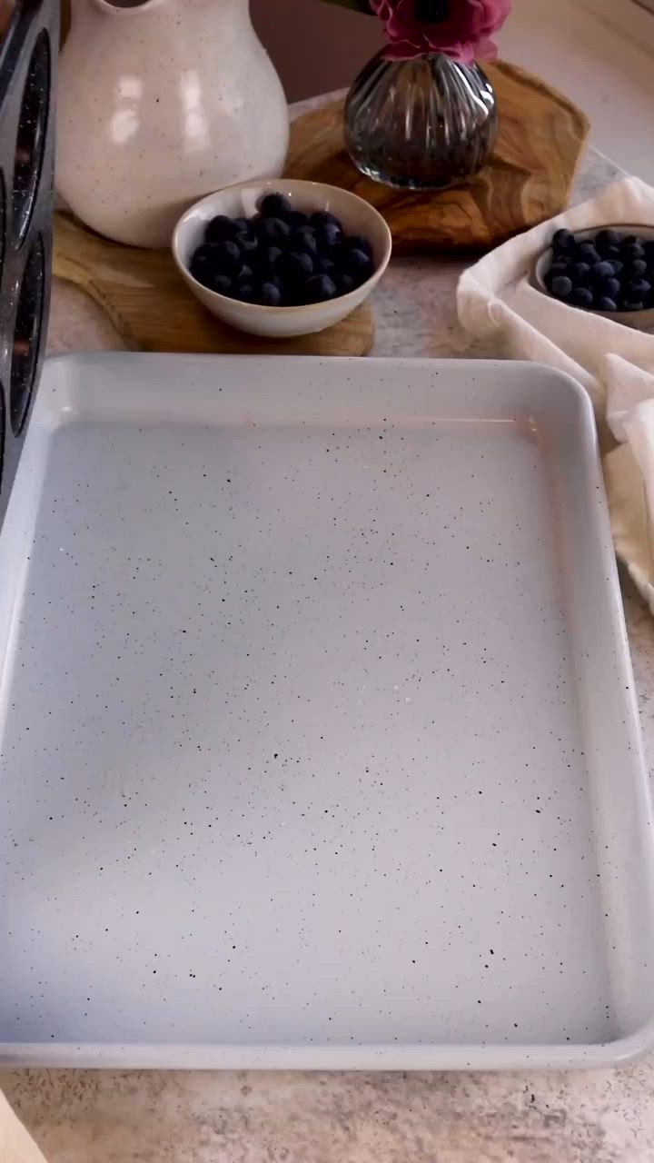 This may contain: a white tray with blueberries in it on a counter next to other bowls and vases