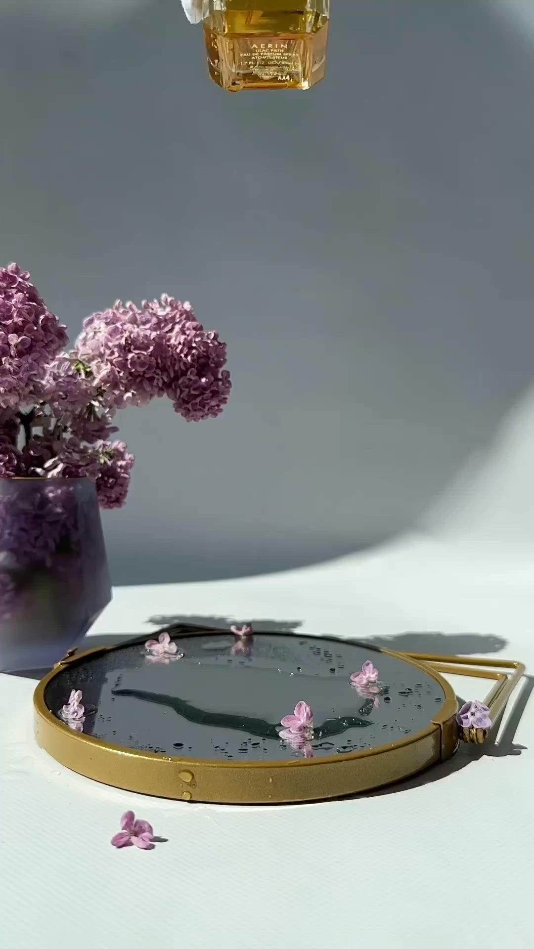 This may contain: a person in white gloves is holding a perfume bottle on a tray with pink flowers