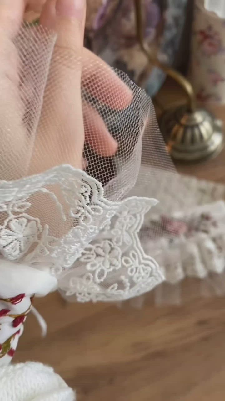 This may contain: two pieces of white lace with pink flowers on them sitting on top of a wooden table