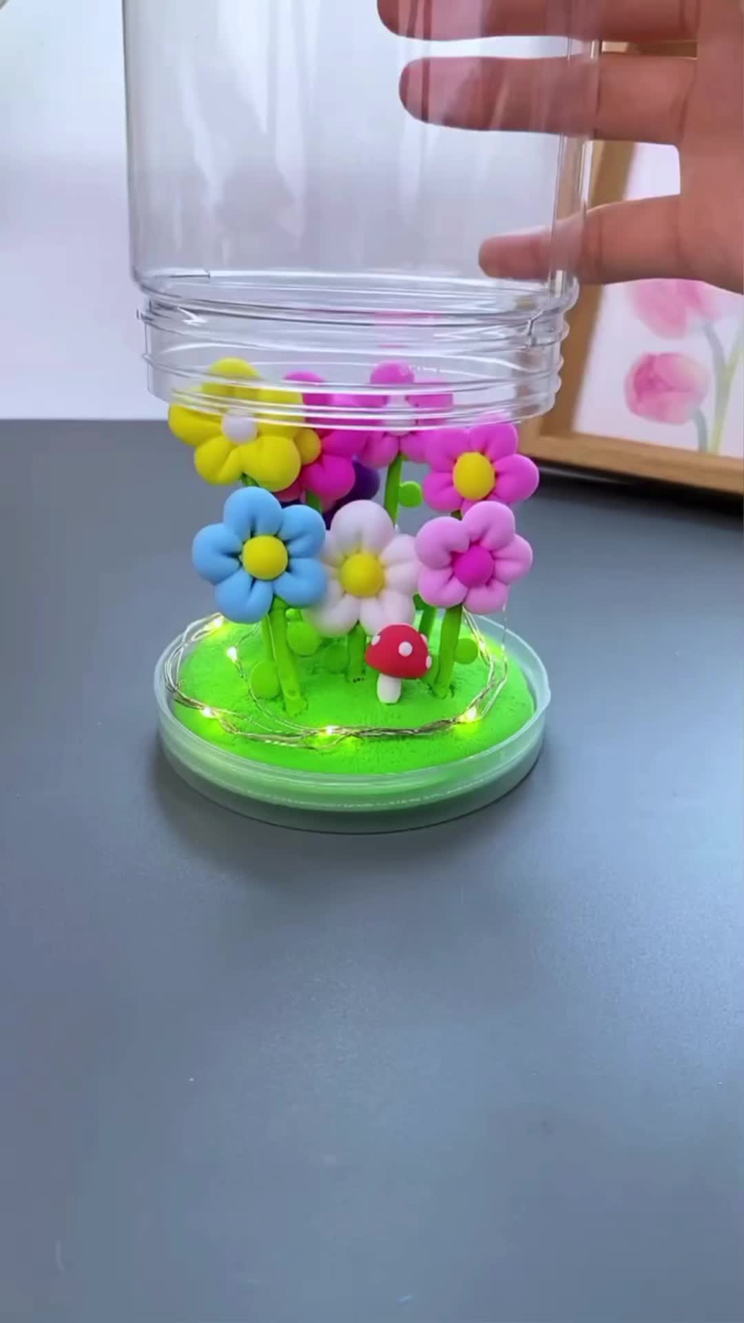 This may contain: a plastic flower arrangement in a glass vase on a table with a hand reaching for it