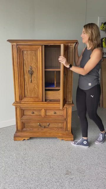 This may contain: a woman standing next to a wooden cabinet in a room with carpeted flooring