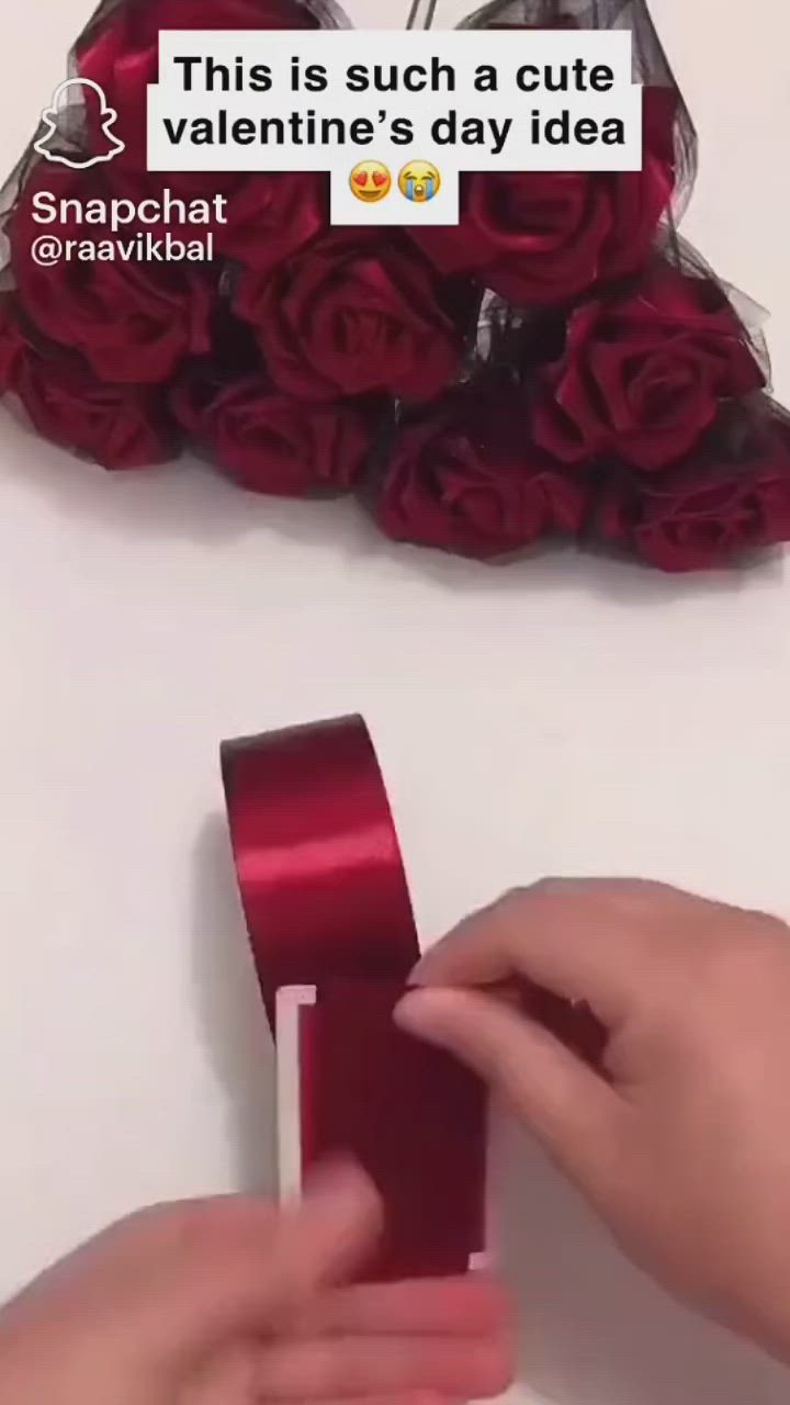 This may contain: someone is holding a red ribbon in front of a bouquet with roses on the wall