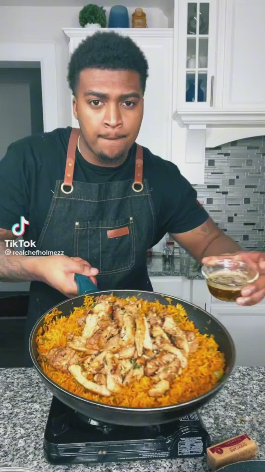 This may contain: a man in an apron pours sauce over a pan filled with rice and meat