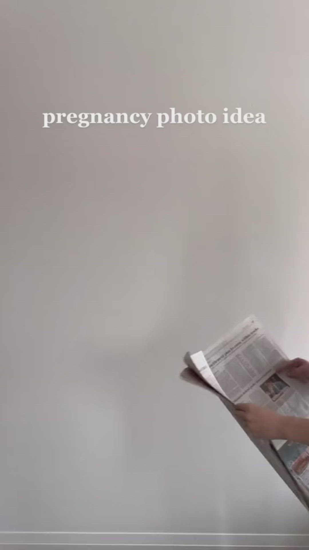 This may contain: a pregnant woman reading a newspaper while leaning against a wall