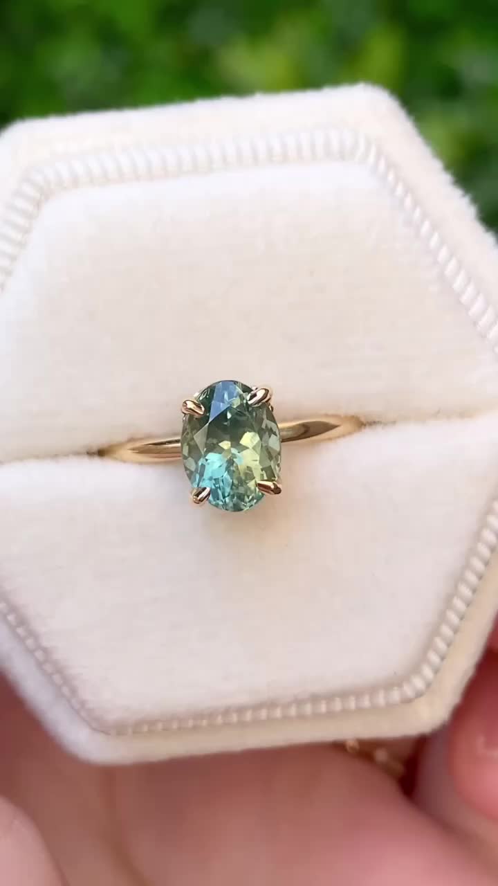 This may contain: a person holding an engagement ring with a blue and green stone in it's center